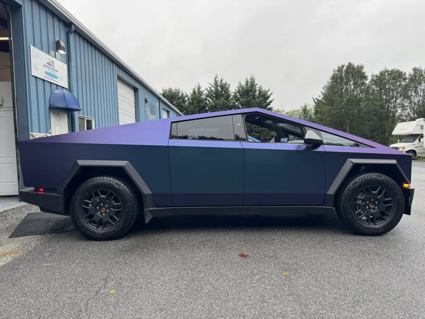 A Cybertruck in a satin color-shift film that reads purple from one angle and blue from another, parked outside the shop