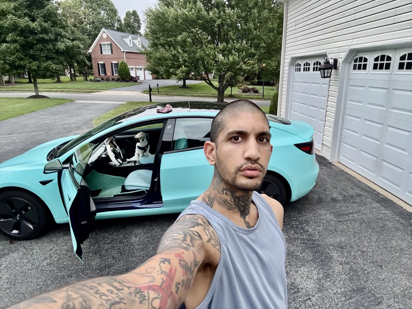 Raoul, the installer, beside the shop’s own Tesla Model 3 wrapped in 3M Satin Key West, driver’s door open, on a driveway
